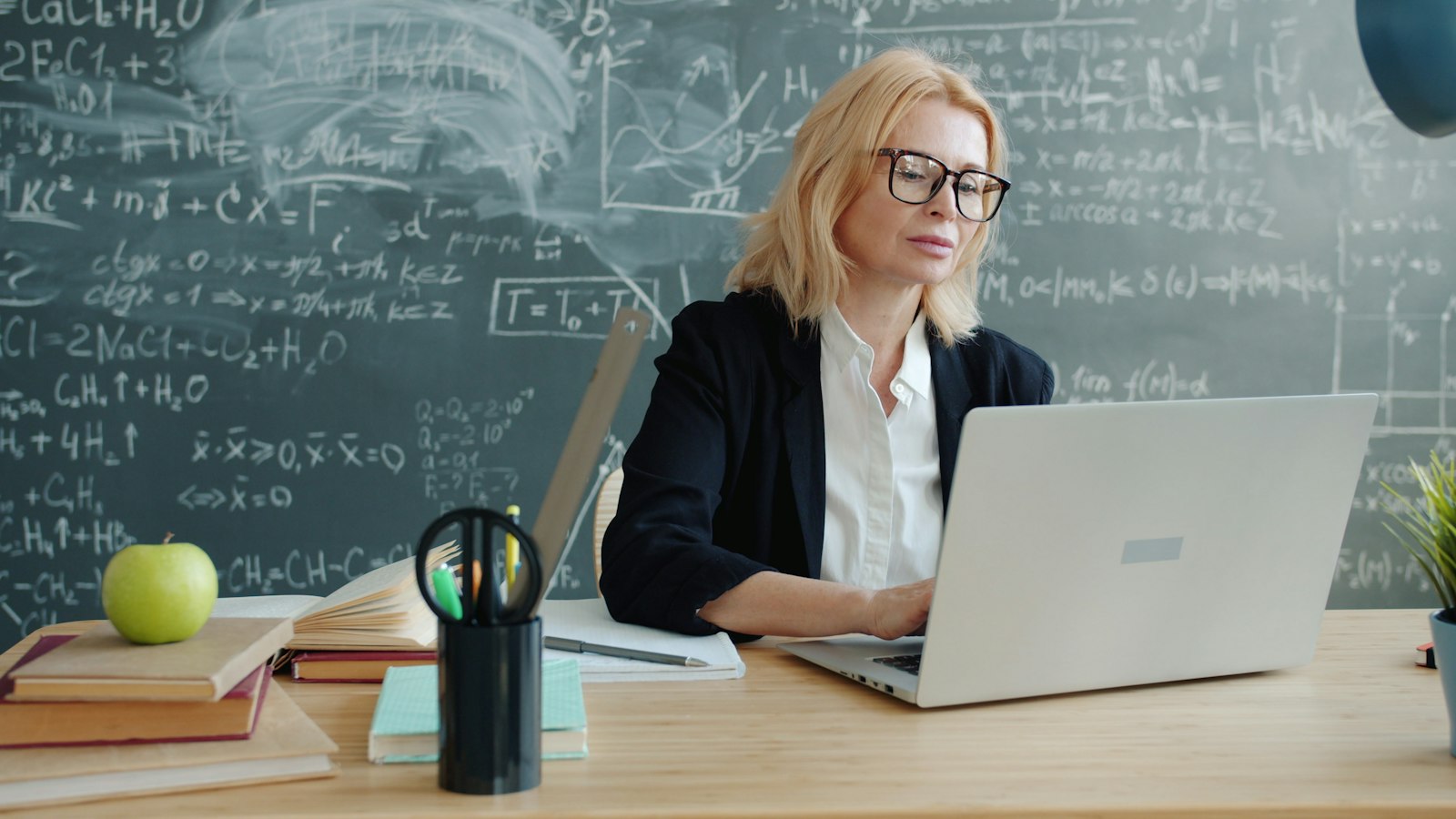 Nauczycielka pracująca na laptopie przy tablicy szkolnej